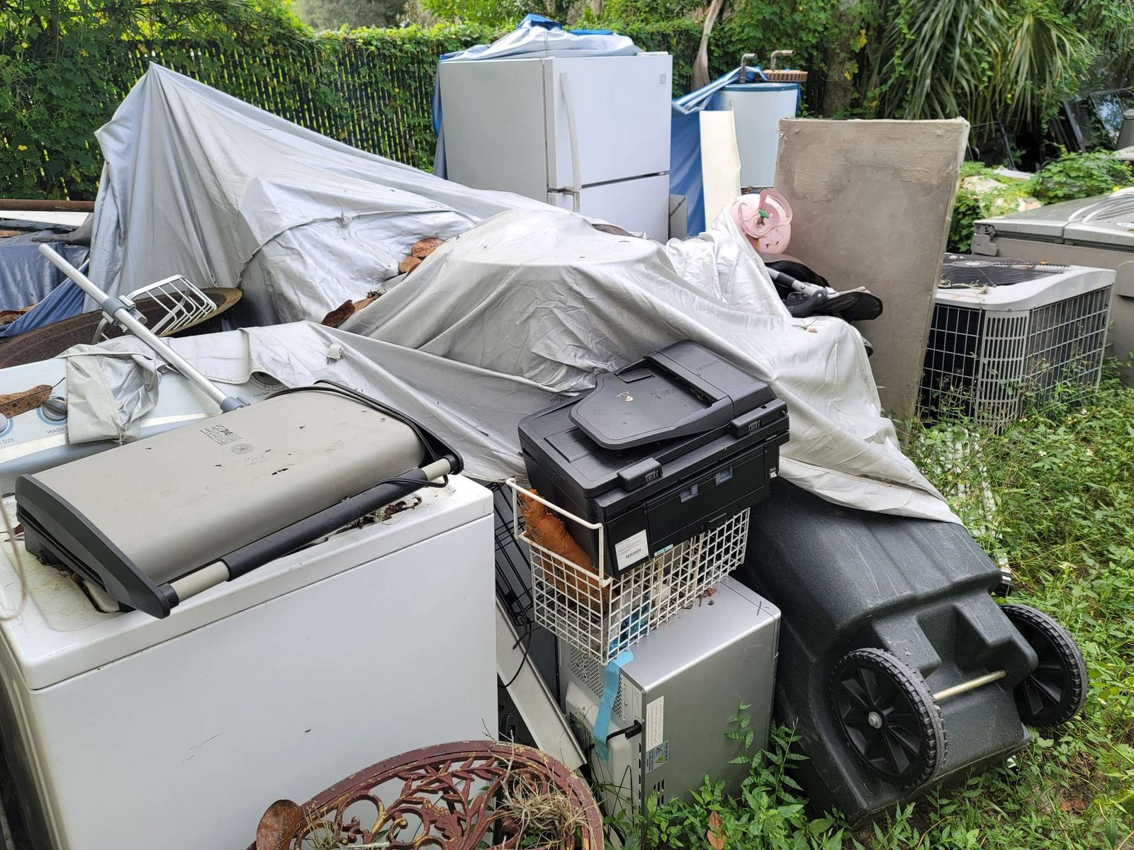 Before: mixed junk pile in yard with appliance, tent, and household items