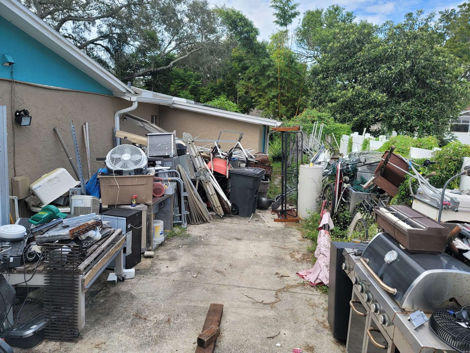 Before: packed side yard with appliances, AC units, and mixed scrap piled along house exterior